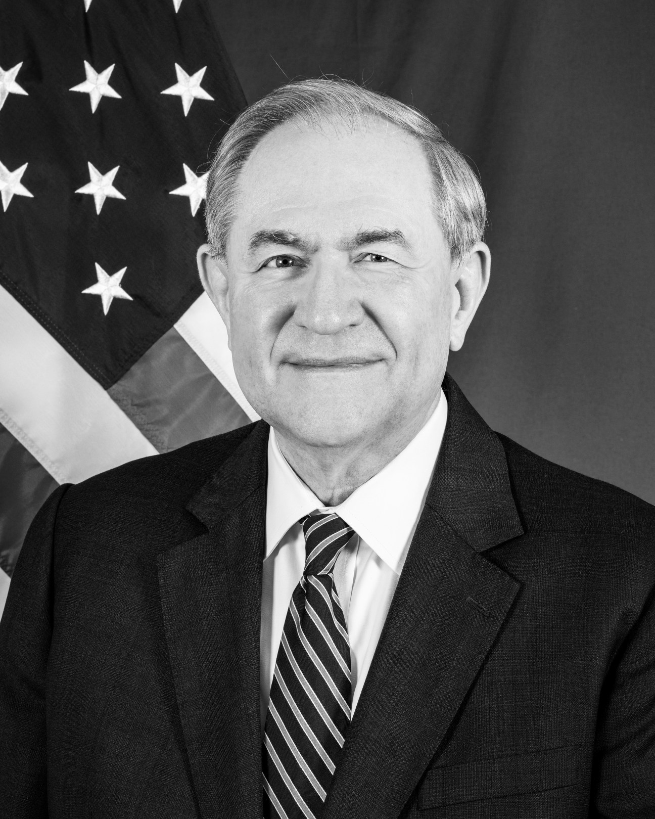 Black and white portrait of James Gilmore in formal attire against American flag background