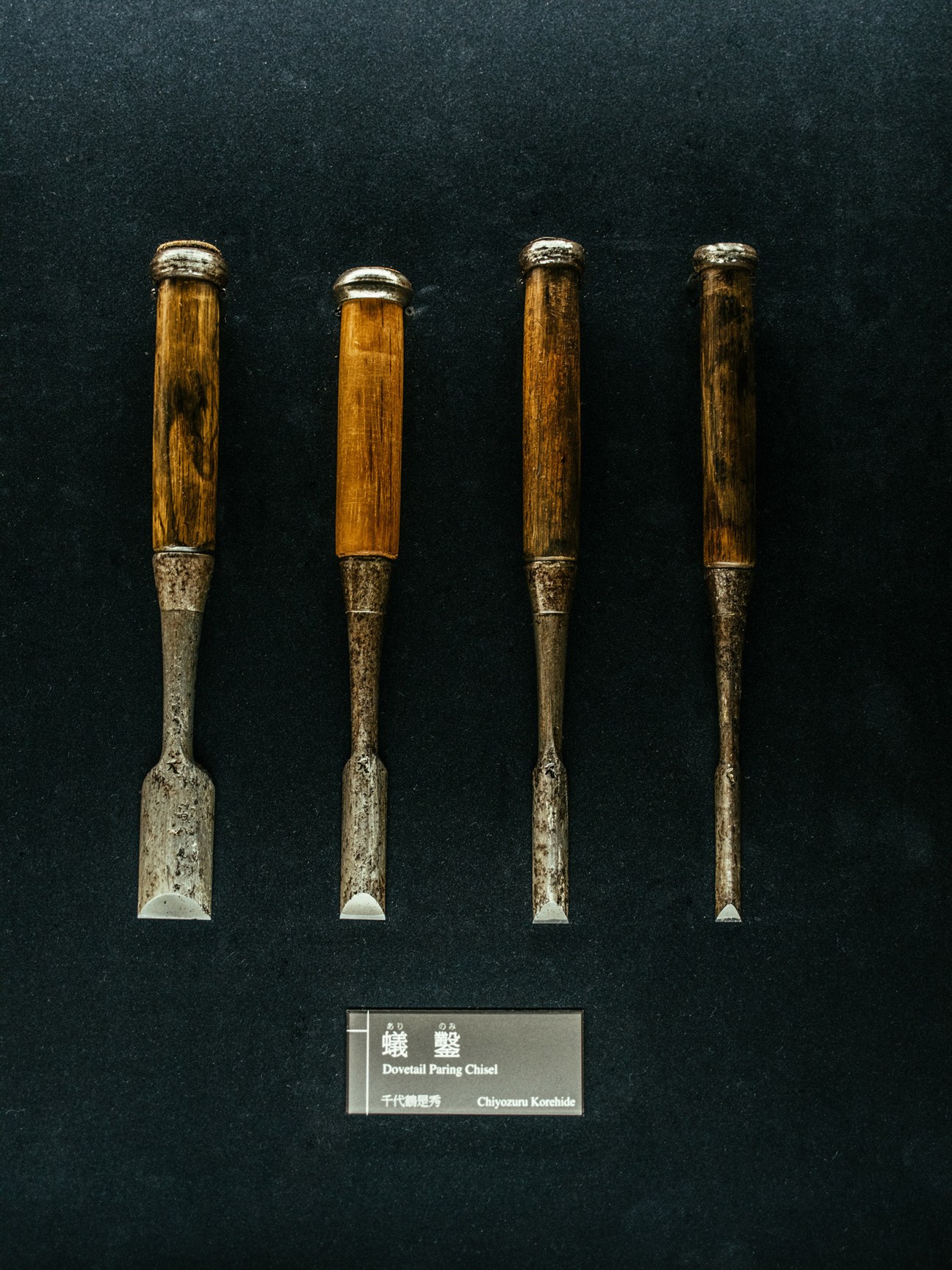 Four traditional Japanese dovetail paring chisels with wooden handles and metal blades displayed against a dark background.