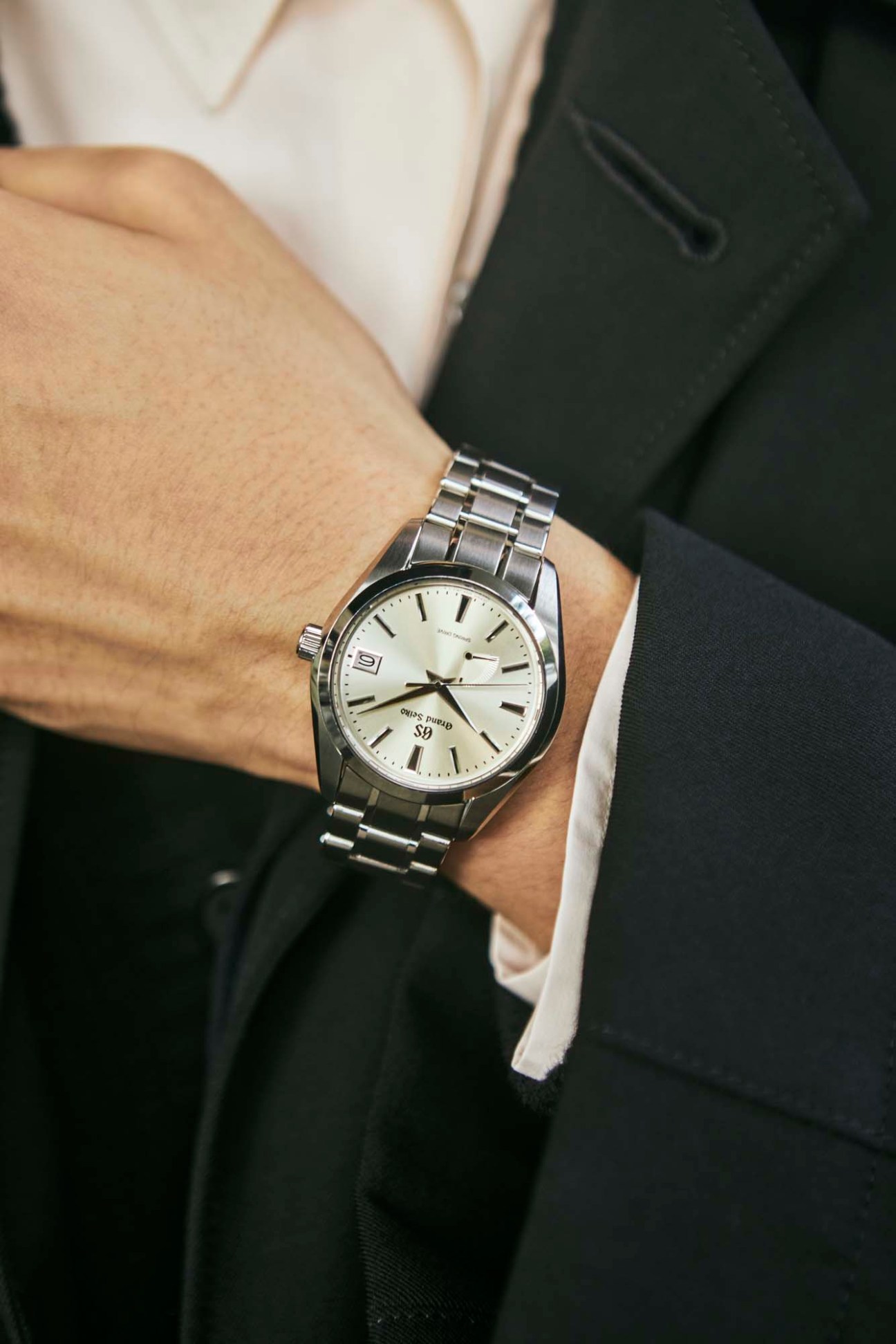 Person wearing stainless steel Grand Seiko watch with white dial and metal bracelet on wrist in business attire