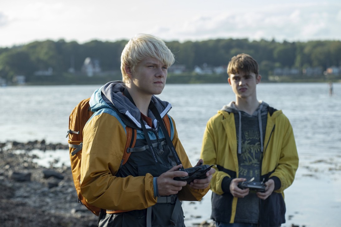 Two young men holding game controllers standing by a lake shore in a scene from Beneath the Surface