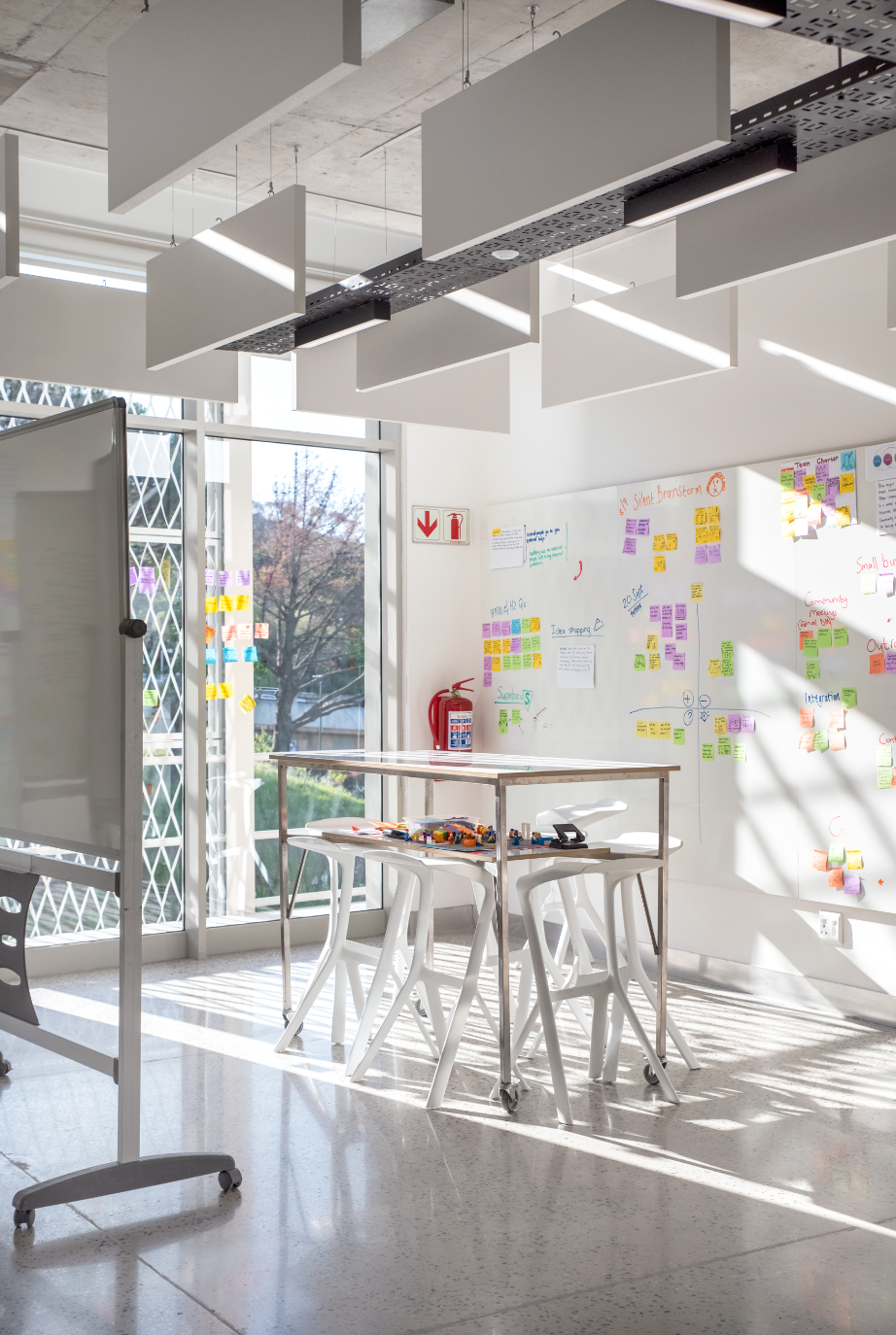Modern design classroom with white walls covered in colorful sticky notes, mobile tables, and large windows