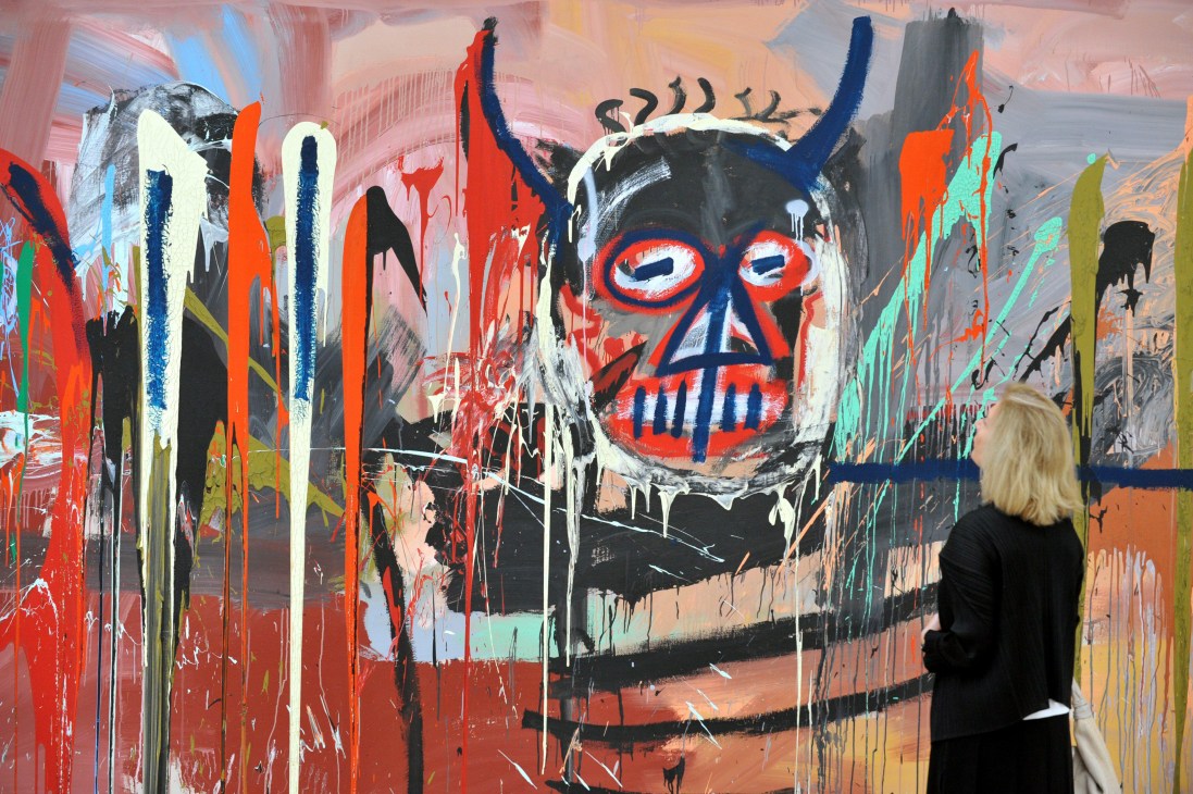 A visitor views a large-scale abstract painting with a horned skull face featuring red and blue markings in vibrant colors.