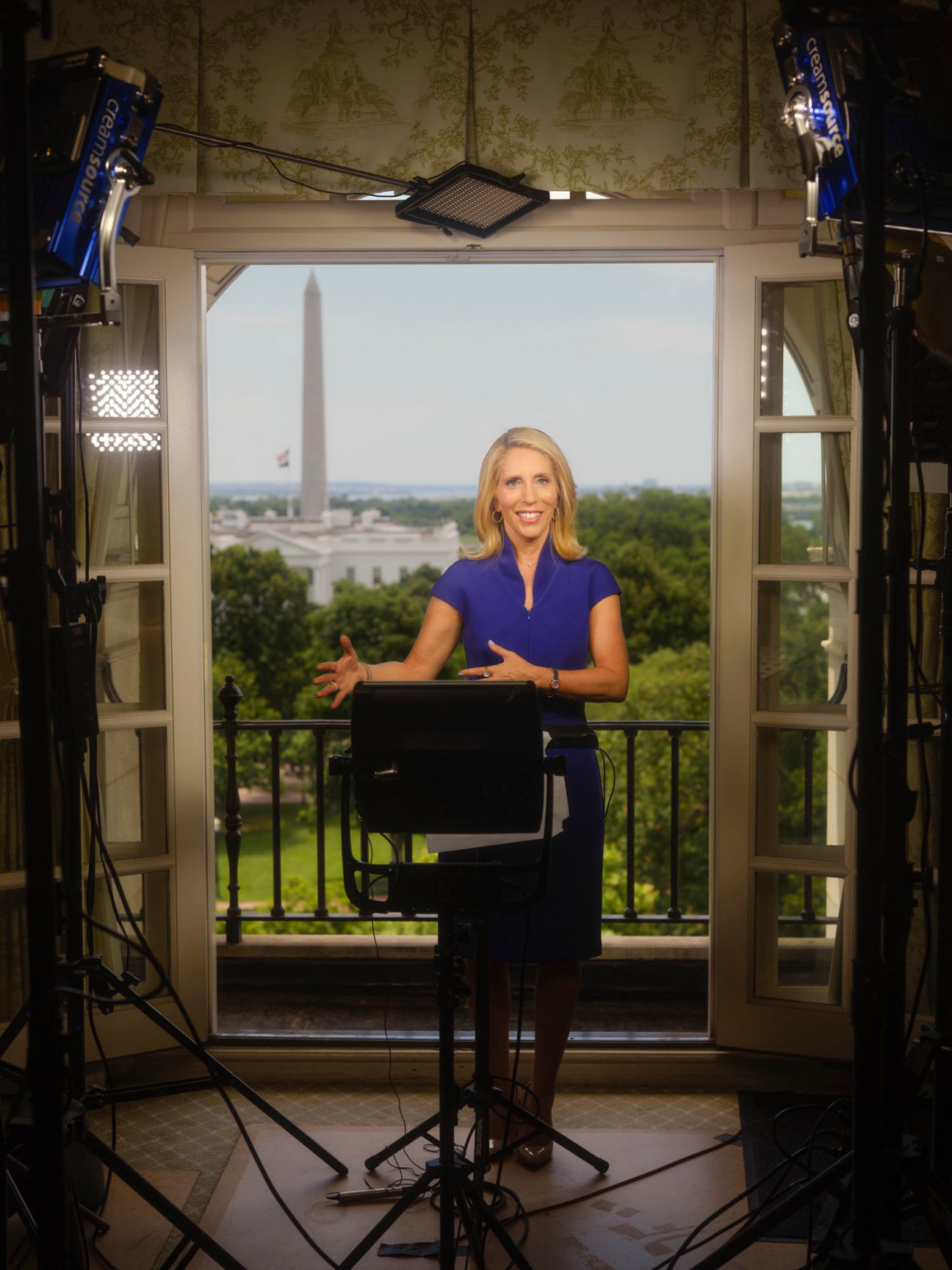 Dana Bash standing at podium in broadcast studio with Washington Monument visible through windows behind her