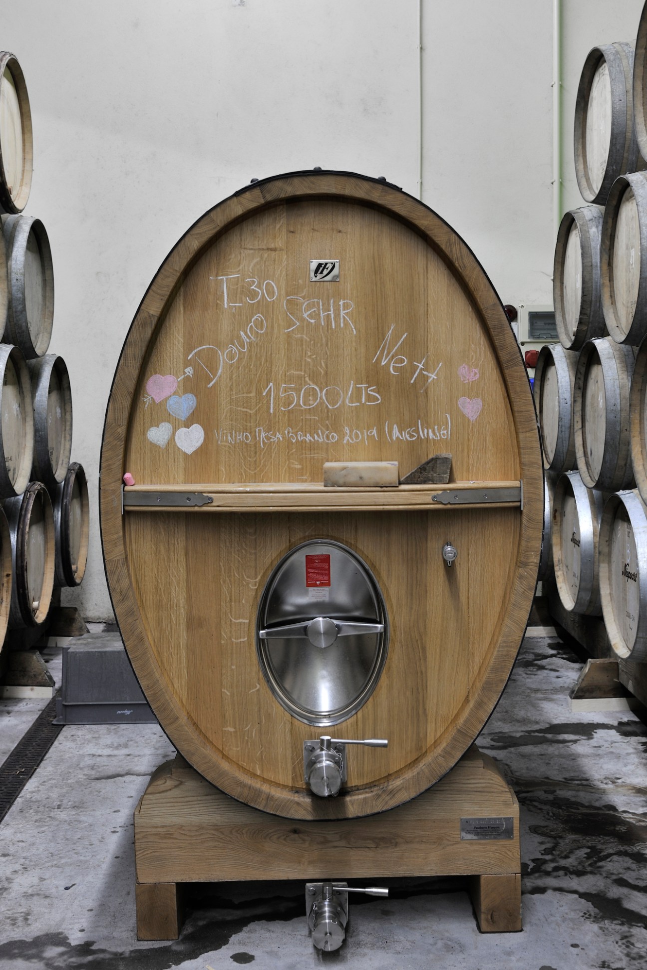 Large wooden wine barrel with chalk writing and decorative hearts, featuring a stainless steel tap at the bottom