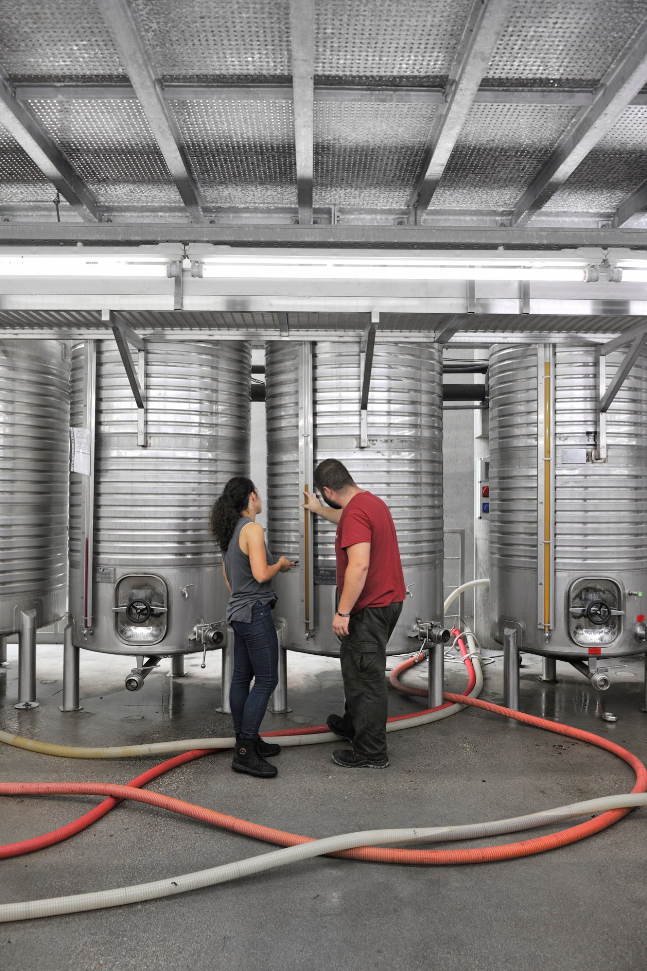 Two workers inspecting stainless steel fermentation tanks at Niepoort winery with hoses on the floor