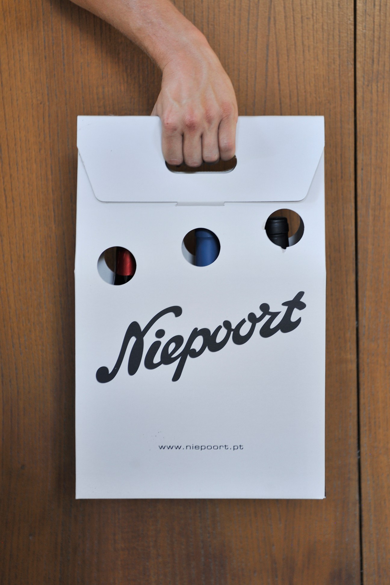 Hand holding white Niepoort wine carrier bag with three circular holes and company logo