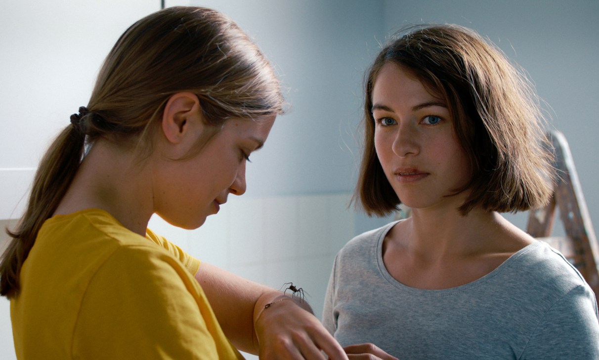 Two young women in casual clothing, one looking down at something on her hand while the other watches