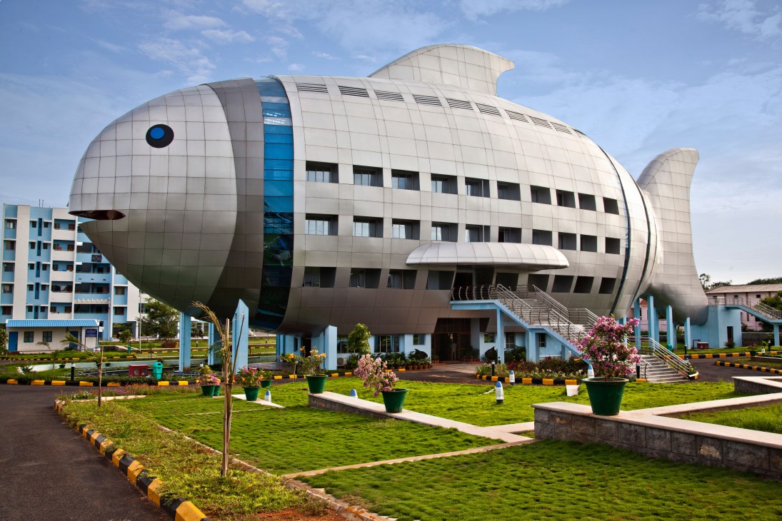 Fish-shaped building with white paneled exterior and windows, surrounded by landscaped grounds