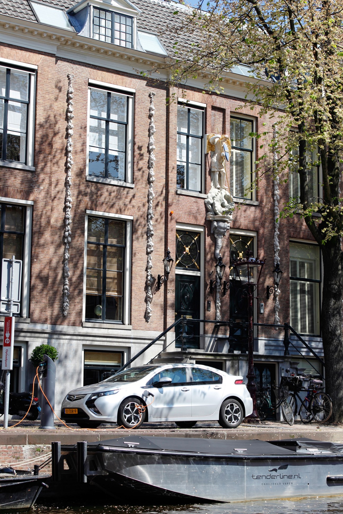 White electric car charging at a station on an Amsterdam street with traditional brick canal houses