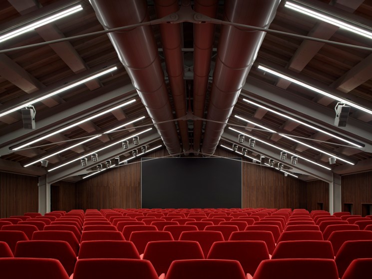 Modern auditorium with red velvet seating and exposed ceiling beams in renovated Procuratie Vecchie building