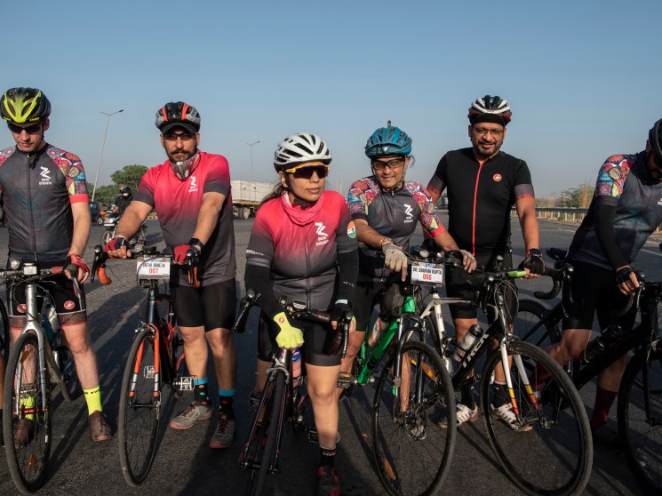 Reena Katyal and fellow Delhi Cyclists members stand with their bikes on a New Delhi highway, wearing helmets and cycling gear.