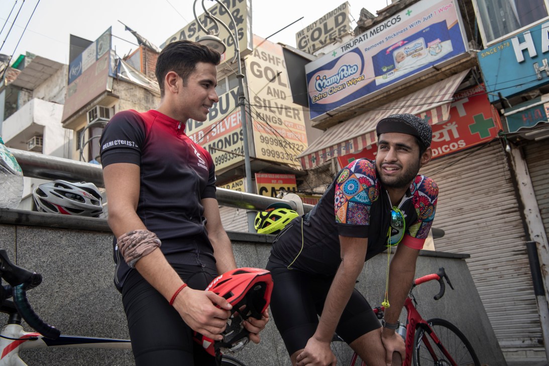 Two cyclists in cycling gear chat while holding helmets on a New Delhi street.
