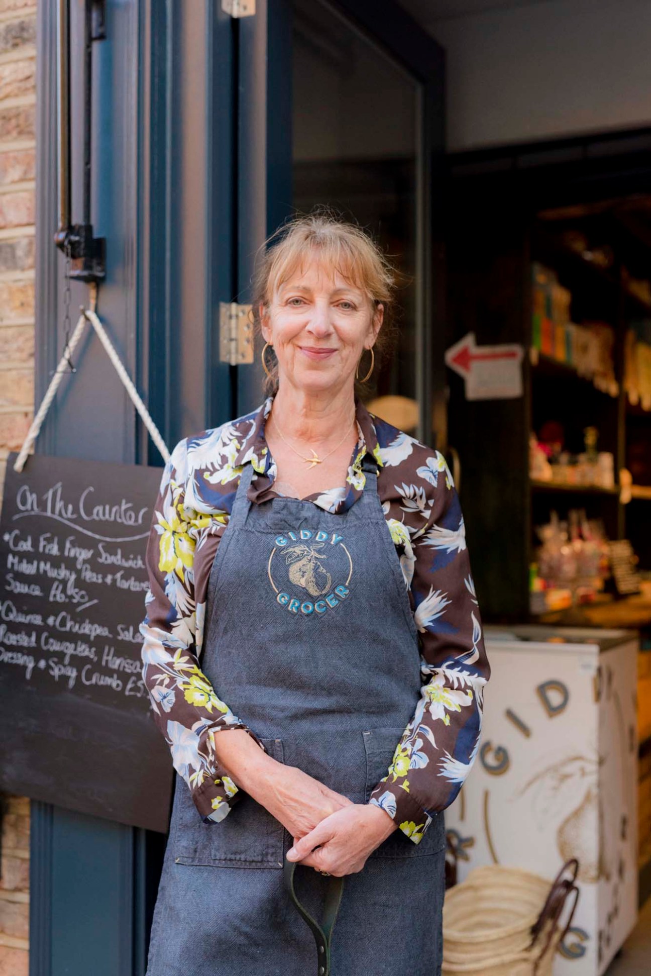 Christine Hall, owner of Giddy Grocer, standing in her shop wearing a Giddy Grocer apron.