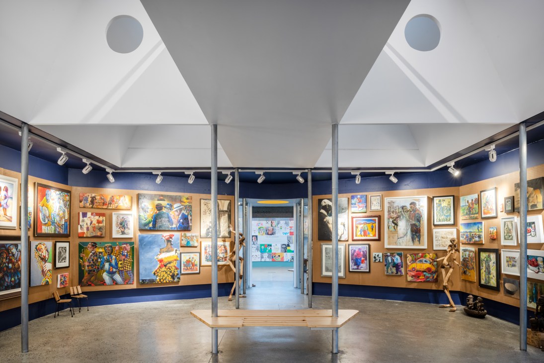 Interior of an art gallery with white walls, ceiling supports, and numerous colorful paintings and artworks displayed