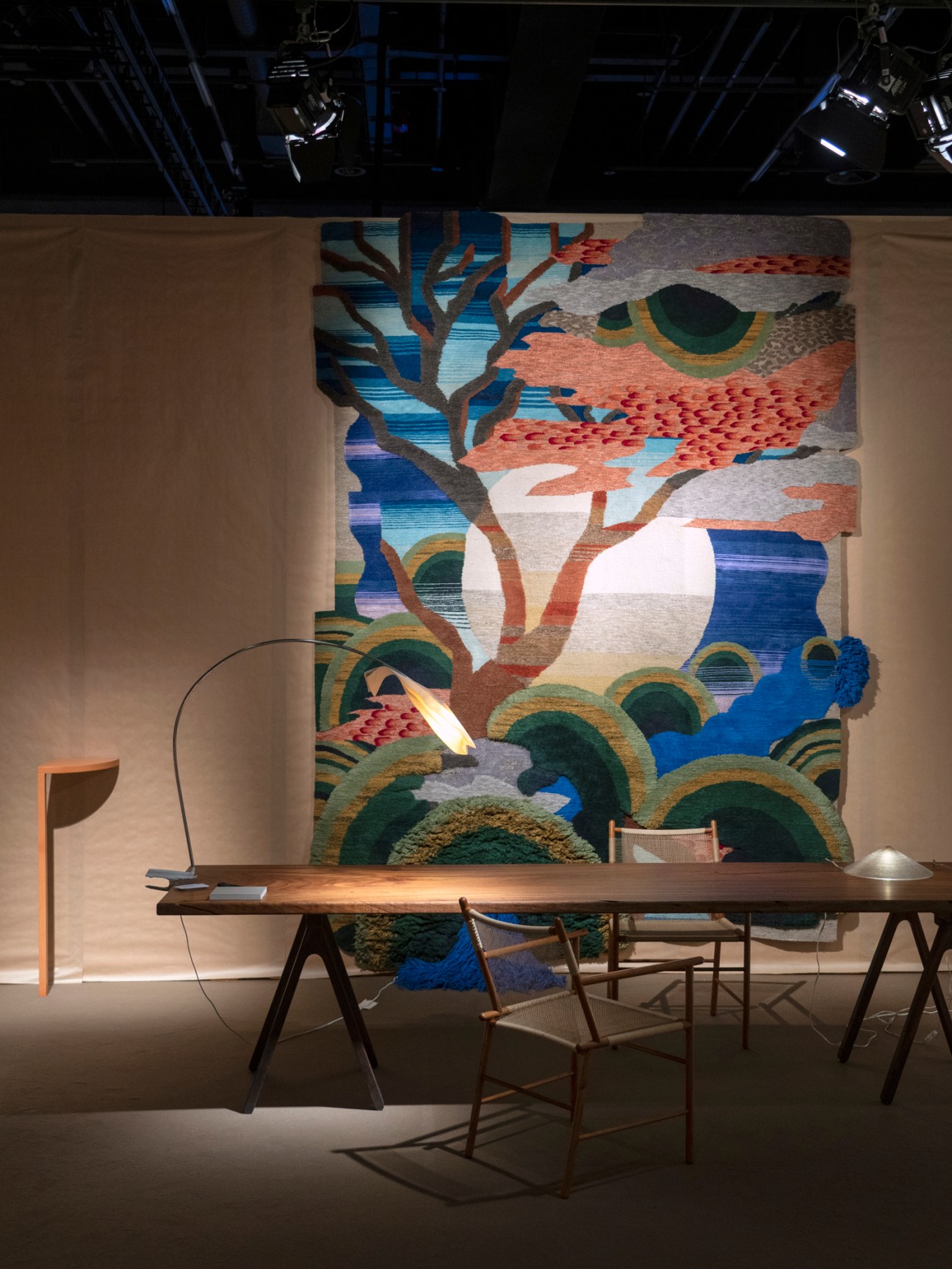 Modern office workspace featuring a wooden trestle desk, designer chairs, and vibrant tapestry artwork