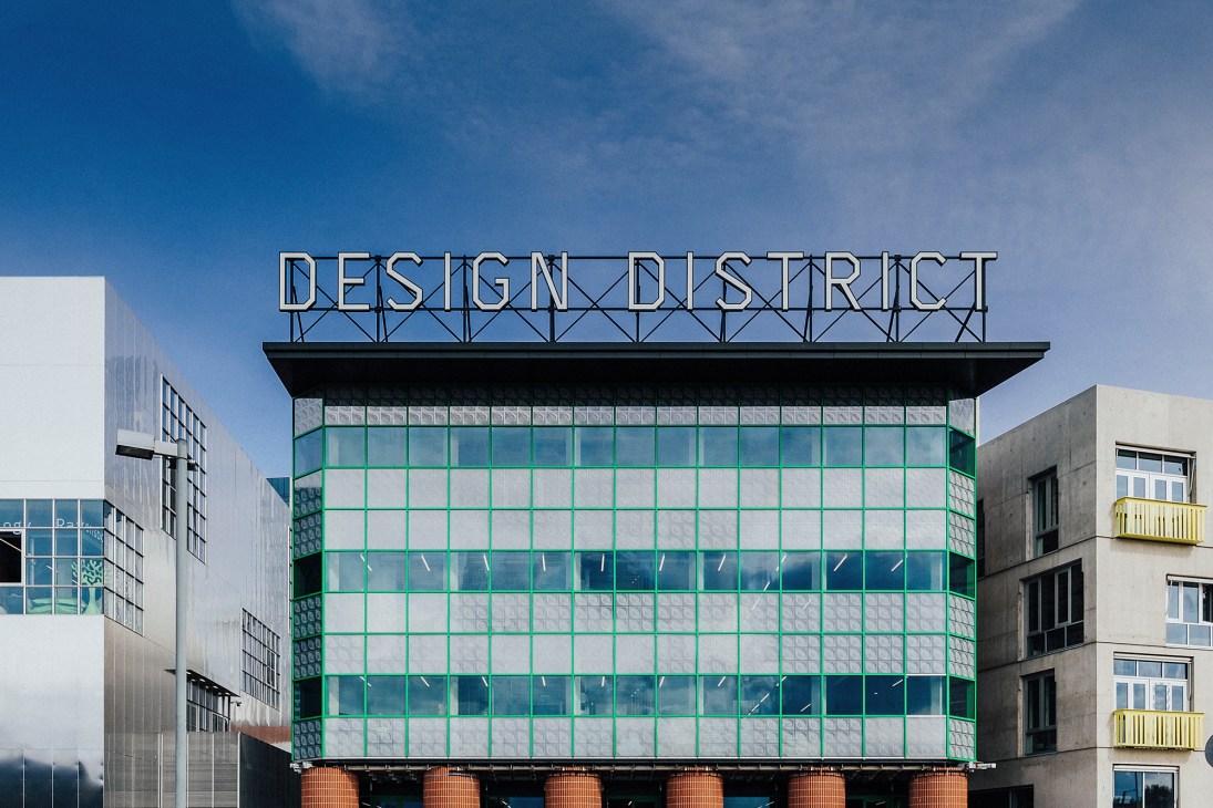 Modern building with green grid facade and 'DESIGN DISTRICT' sign on top surrounded by other contemporary structures