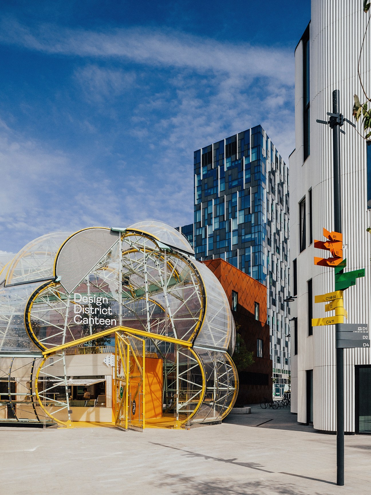 Modern glass and steel buildings with a transparent dome-like canteen structure labeled Design District Canteen