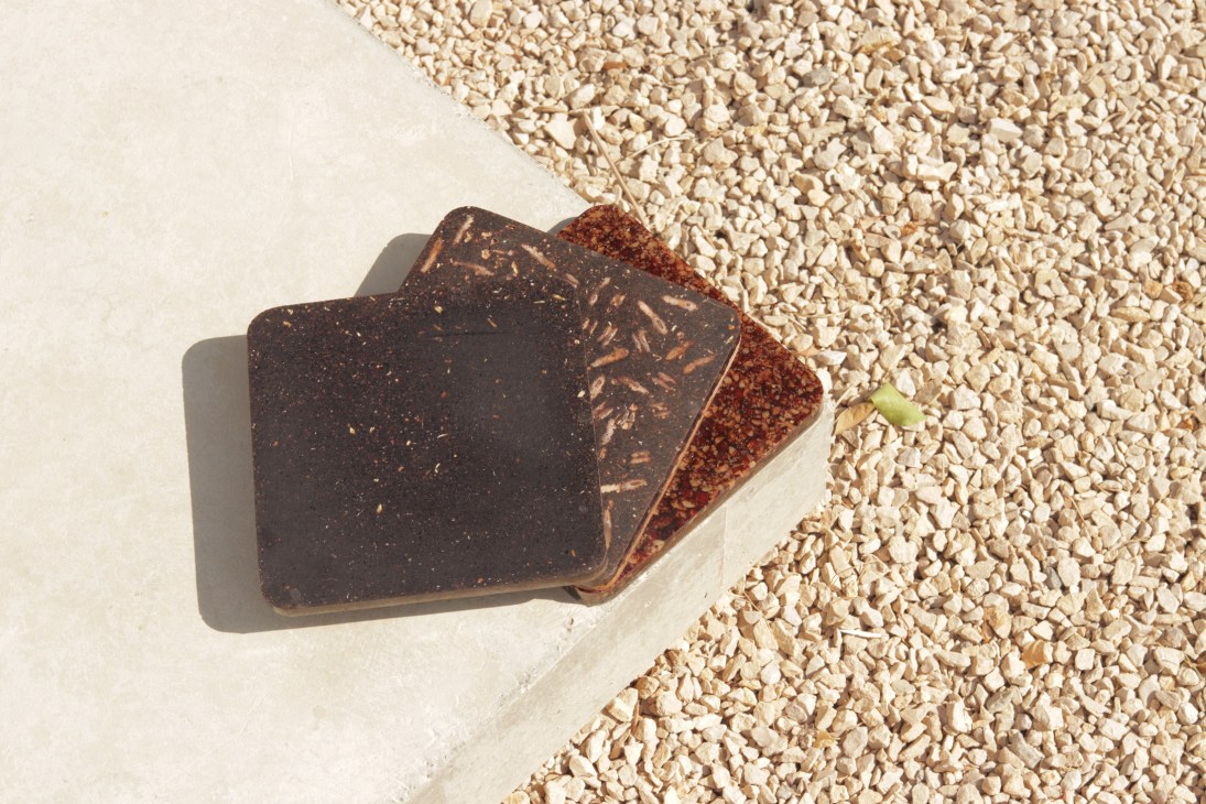 Two material samples made from date seeds, showing dark brown finished product and reddish-brown powder on white gravel background.