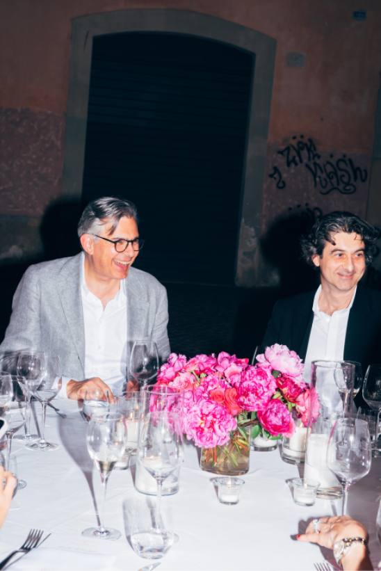 A group of elegantly dressed people seated around a dinner table at an intimate restaurant setting