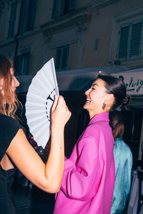 Two well-dressed individuals meeting and shaking hands at what appears to be a social gathering
