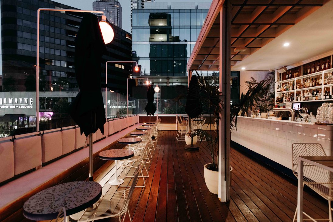 Dom's Social Club rooftop bar in Melbourne with city skyline views, timber decking, pink banquettes and bar counter.