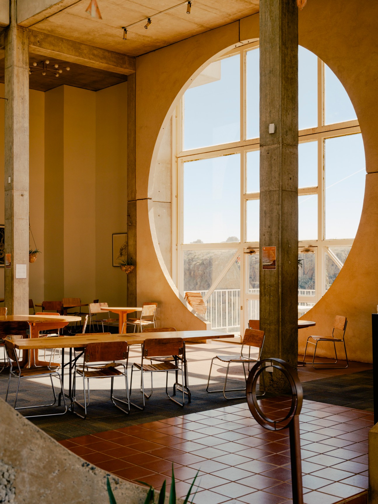 Interior of Arcosanti Café with ochre walls, large circular window, wooden furniture, and desert landscape view.