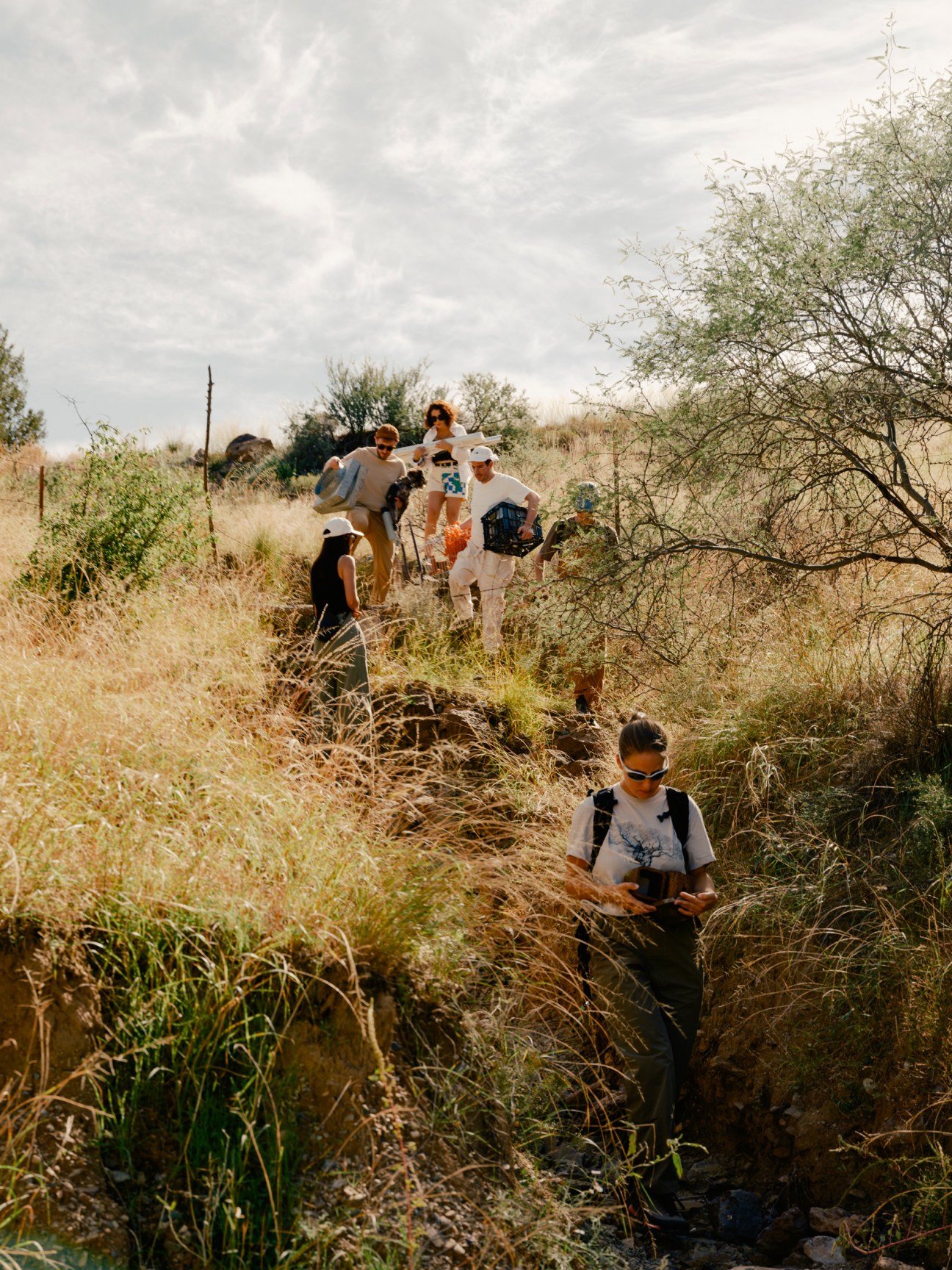 Architecture students hiking through a dry riverbed carrying salvaged building materials in central Arizona.