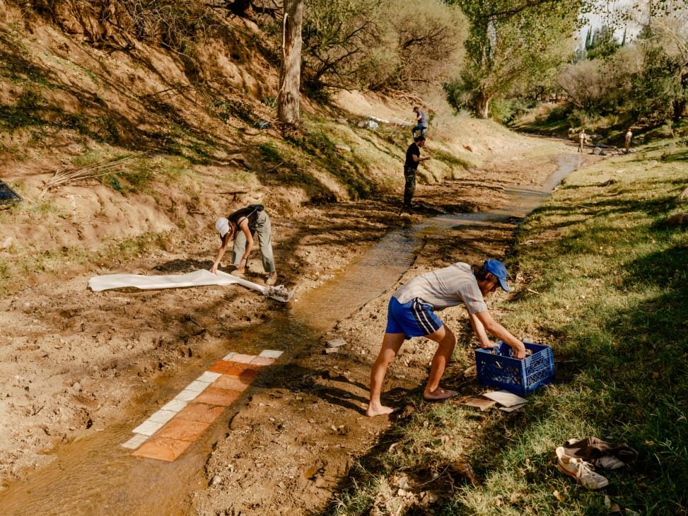 Architecture students work with salvaged materials in a shallow river during an outdoor workshop in the Arizona desert.
