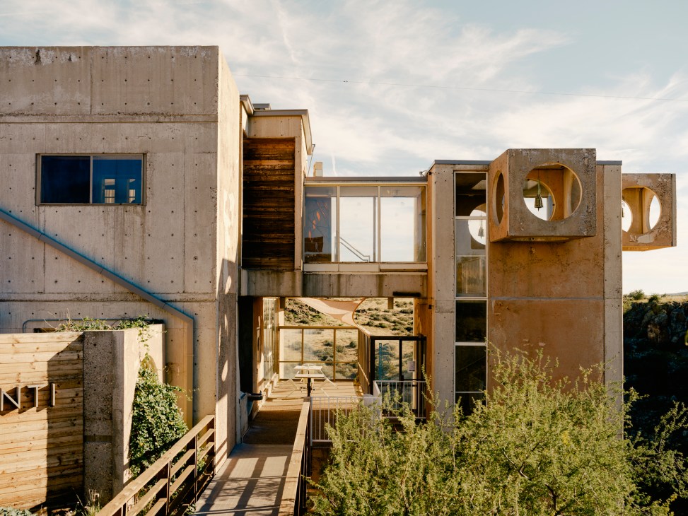 Arcosanti visitor centre with concrete and earth-cast architecture featuring circular openings, wooden elements, and desert landscape views.