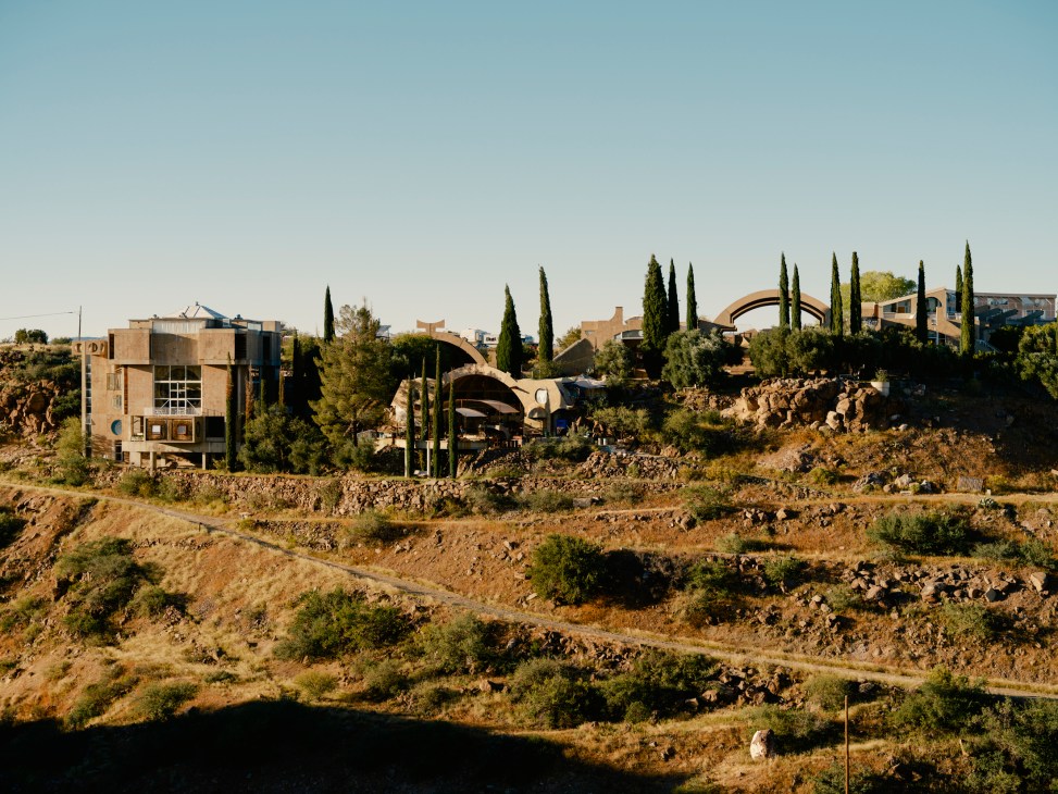 Arcosanti's distinctive architecture with curved concrete structures and cypress trees on a desert hillside.
