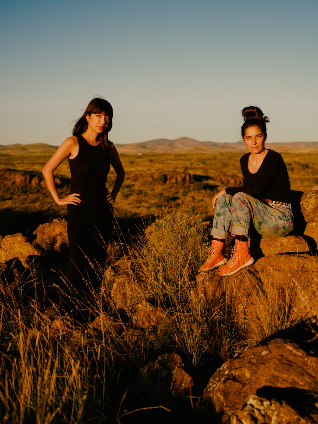Architecture students Stephanie Lin and Théodora Barat stand in a sparse desert landscape with golden rocks and dry vegetation.