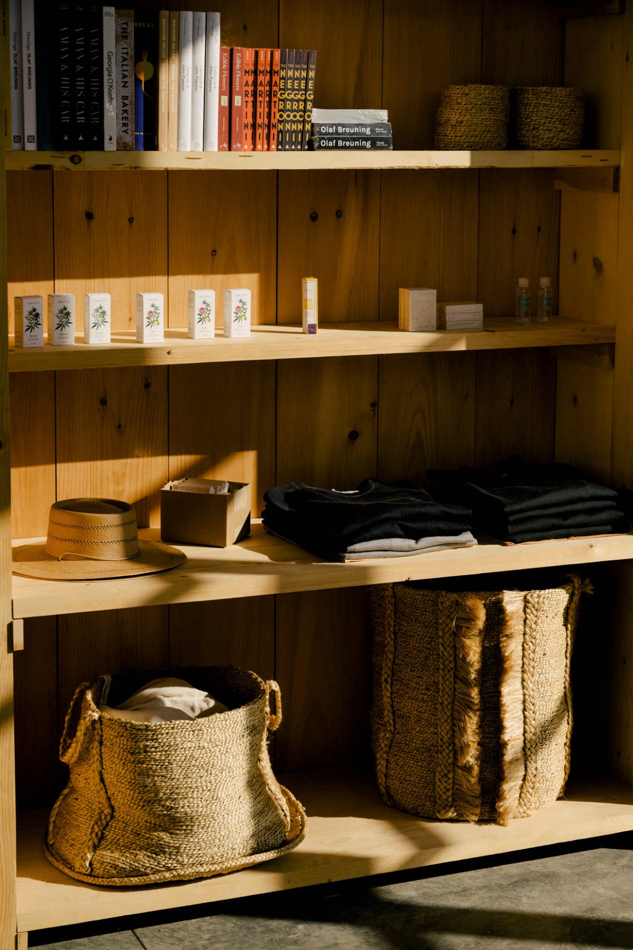 Wooden shelving unit with books, woven baskets, folded clothing, small gift boxes, and a straw hat
