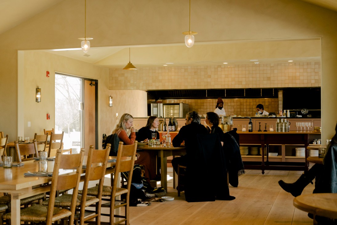 Interior of restaurant with diners seated at tables and bar, open kitchen visible in background