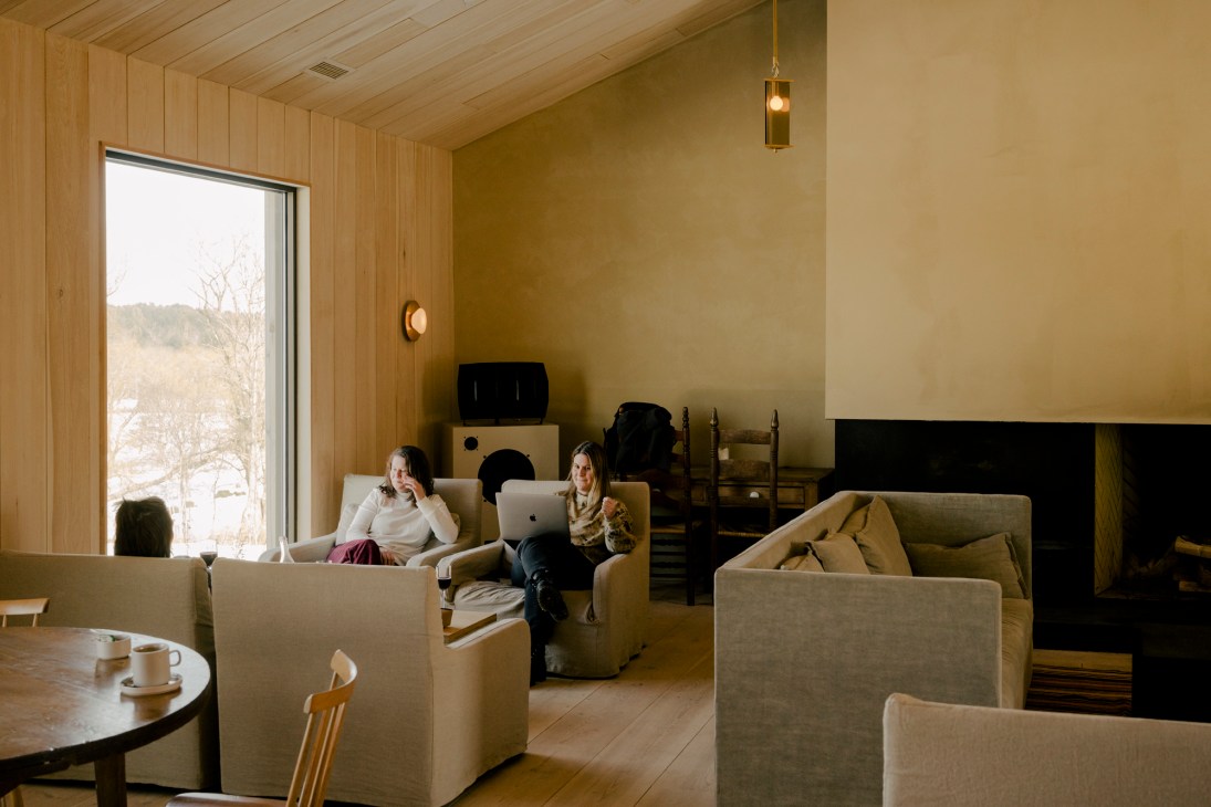 Two people working on laptops in a modern lounge with wood paneling, beige furniture and a fireplace