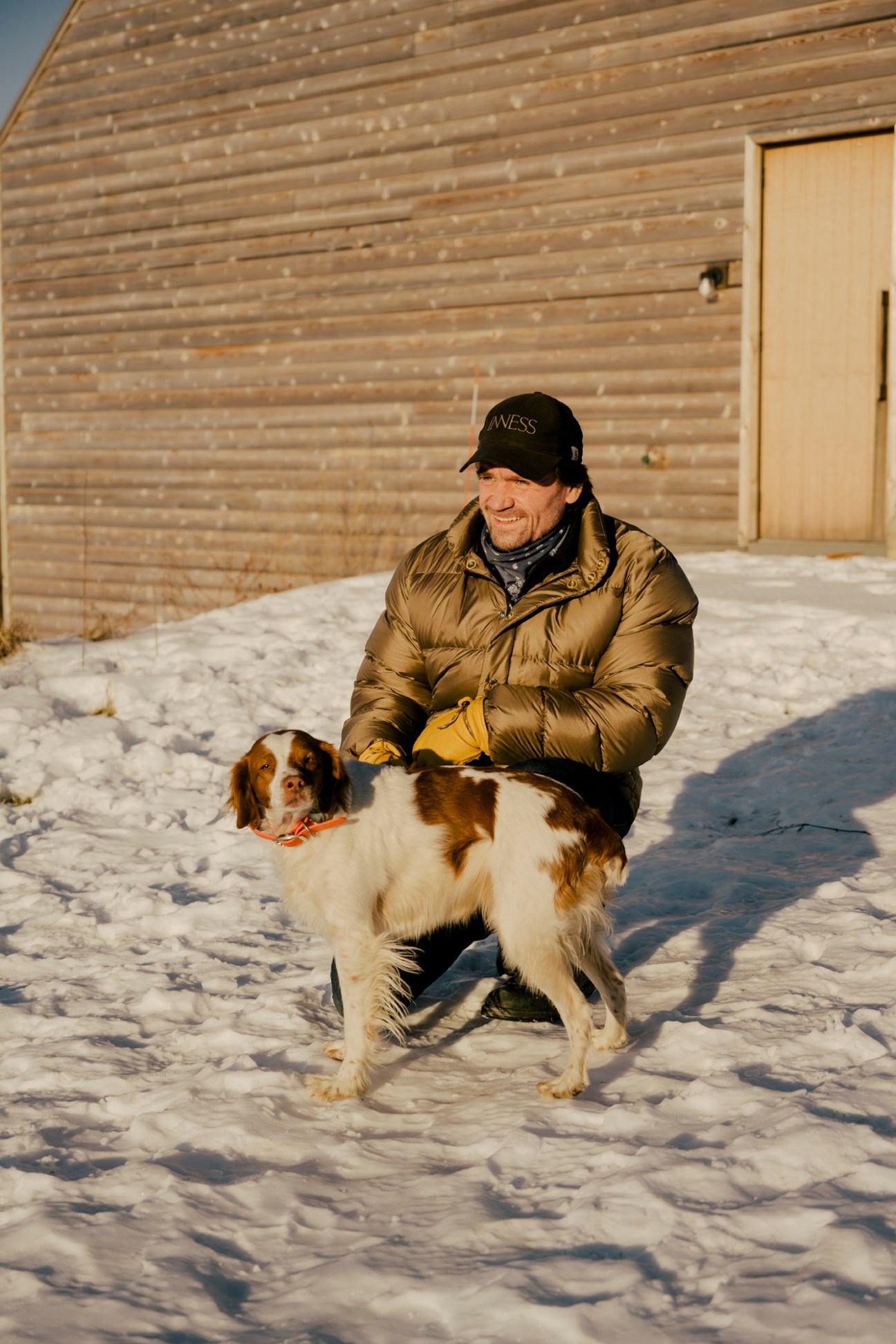 Taavo Somer crouching in snow with his dog outside a wooden building