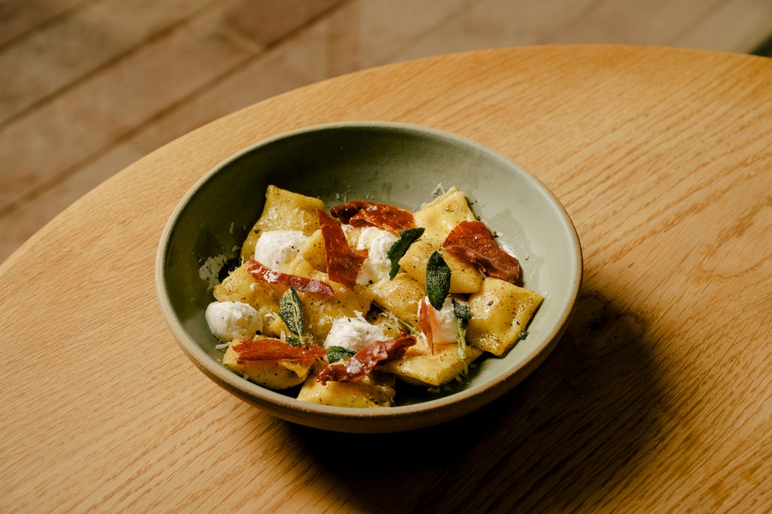 Pasta with crispy pancetta, mozzarella, sage leaves and black pepper in a ceramic bowl on wooden table
