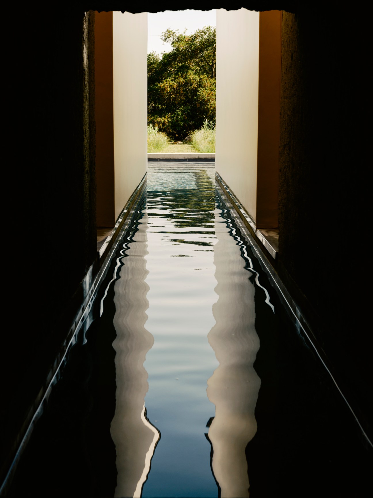 Narrow water channel viewed through concrete opening leading toward house sanctuary with reflective surface