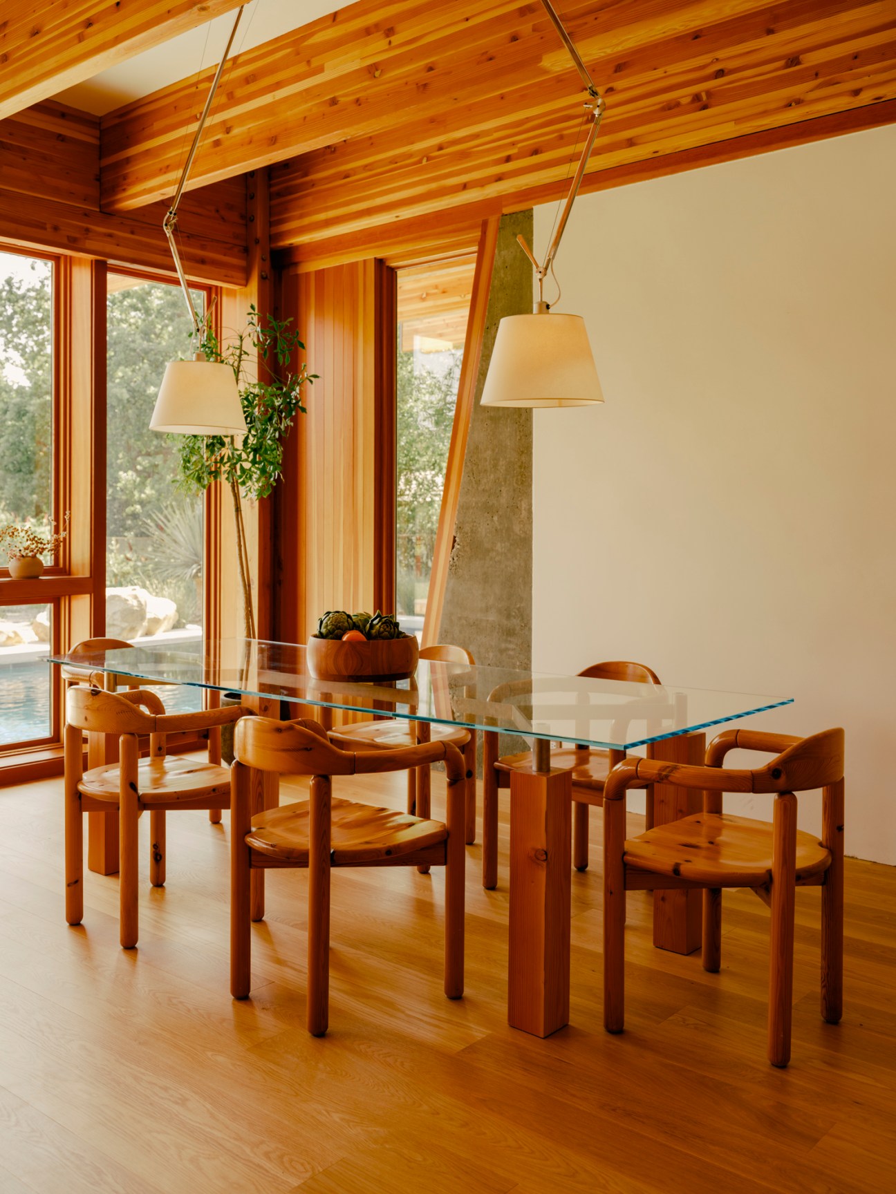 Dining room with glass-topped table surrounded by wooden chairs under pendant lights with exposed ceiling beams