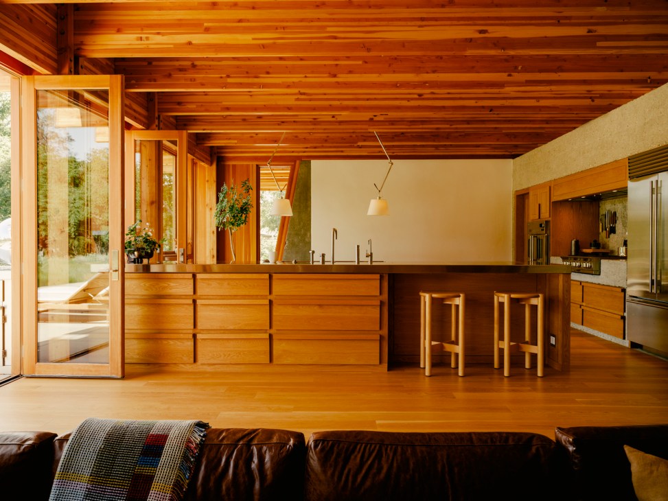 Modern kitchen with warm wood cabinetry, exposed ceiling beams, and concrete countertops with natural lighting