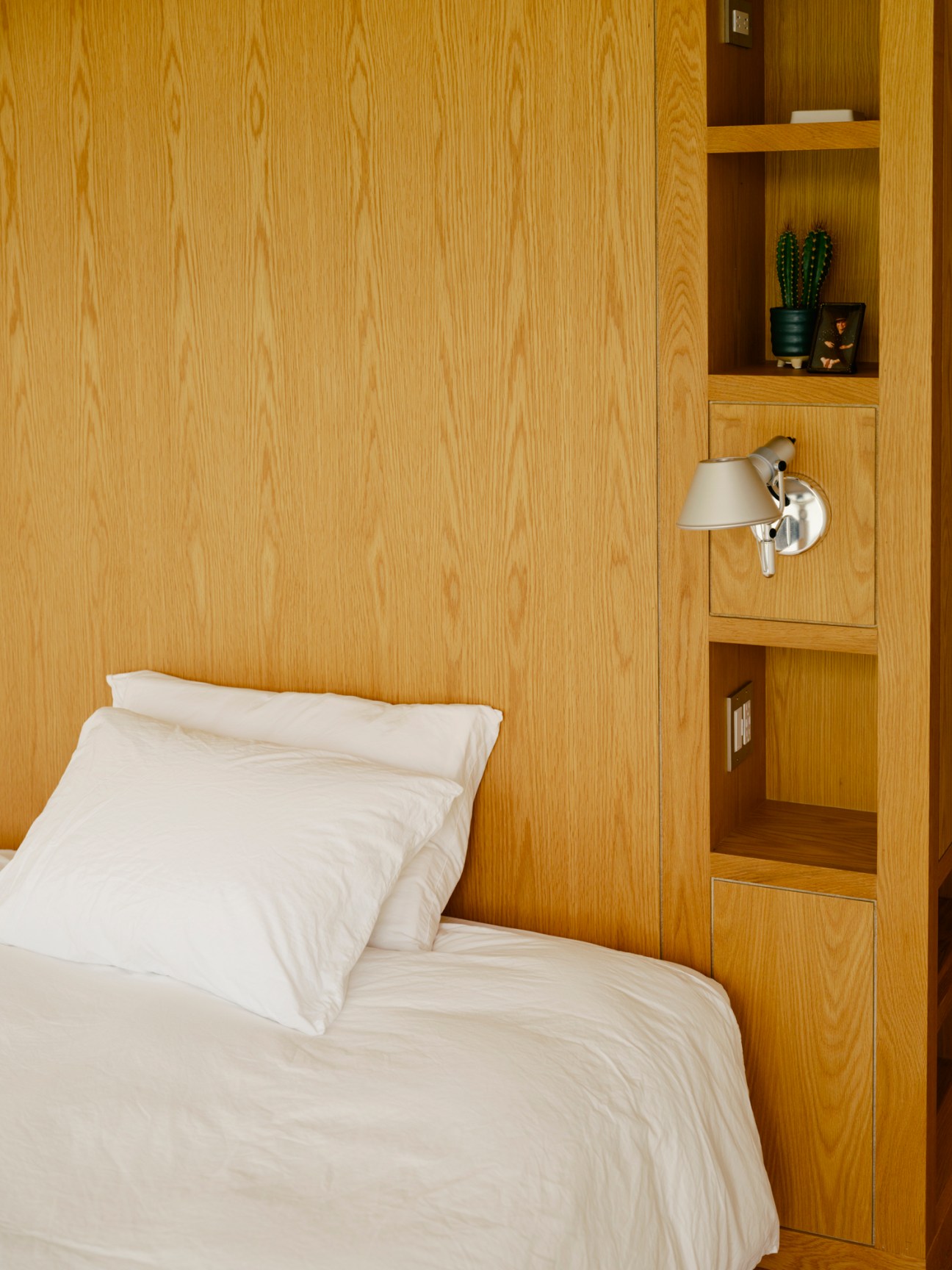 Built-in wooden bedroom furniture with shelving, drawers and mounted reading light in warm oak finish