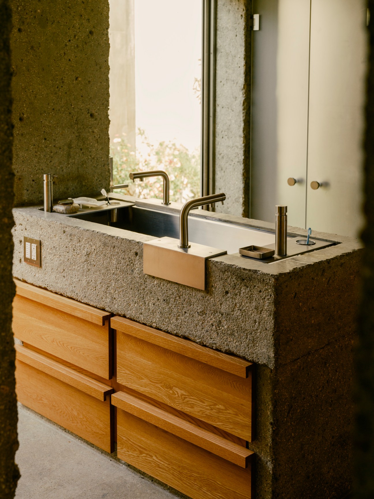 Modern bathroom with dual concrete sinks, brass faucets and warm oak wood cabinetry beneath