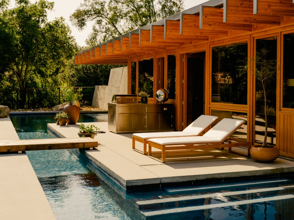 Modern wooden poolside deck with lounge chairs and glass pavilion structure surrounded by trees