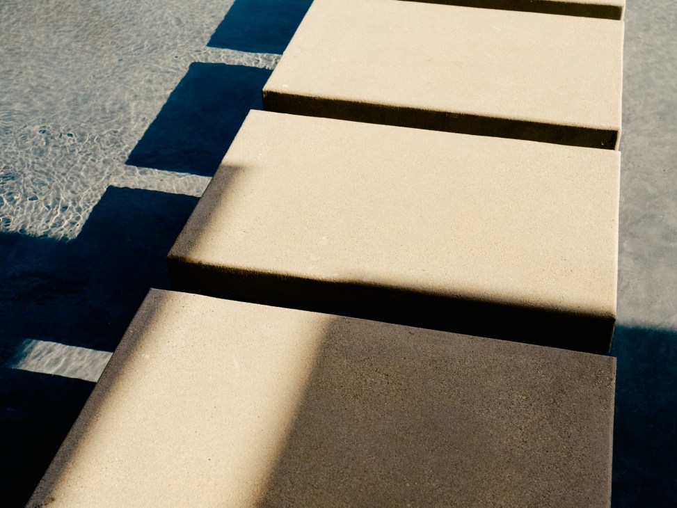 Concrete stepping stones casting shadows over water feature in modernist garden design