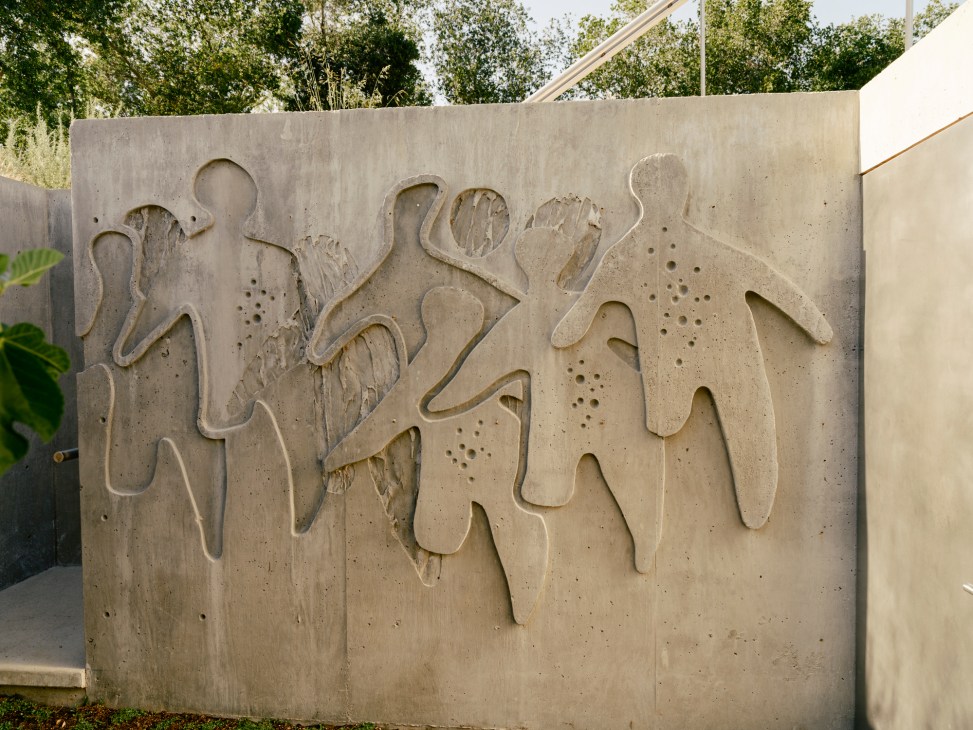 Concrete wall with carved relief showing abstract human figures in flowing, artistic forms