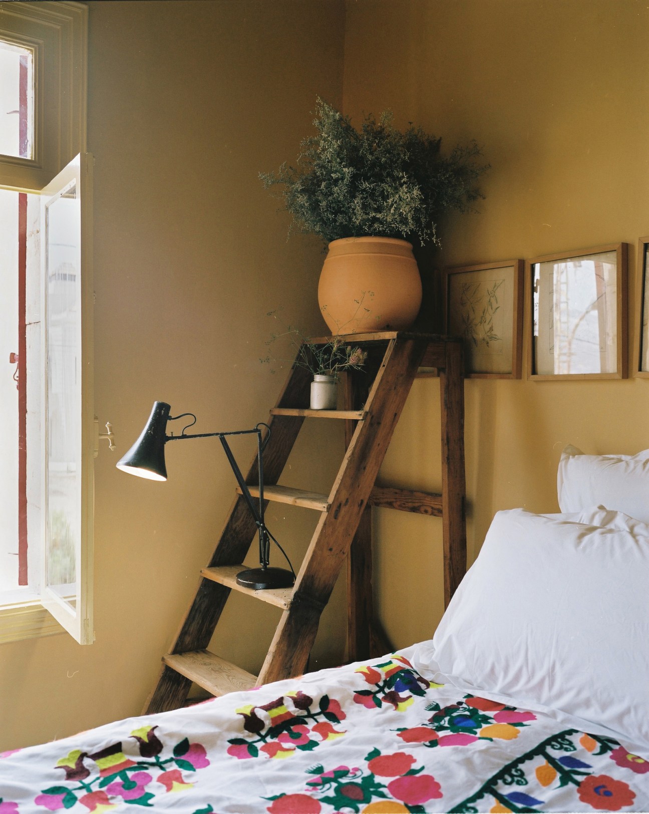 Bedroom with colorful floral bedding, wooden ladder shelf, terracotta pot, and yellow painted walls