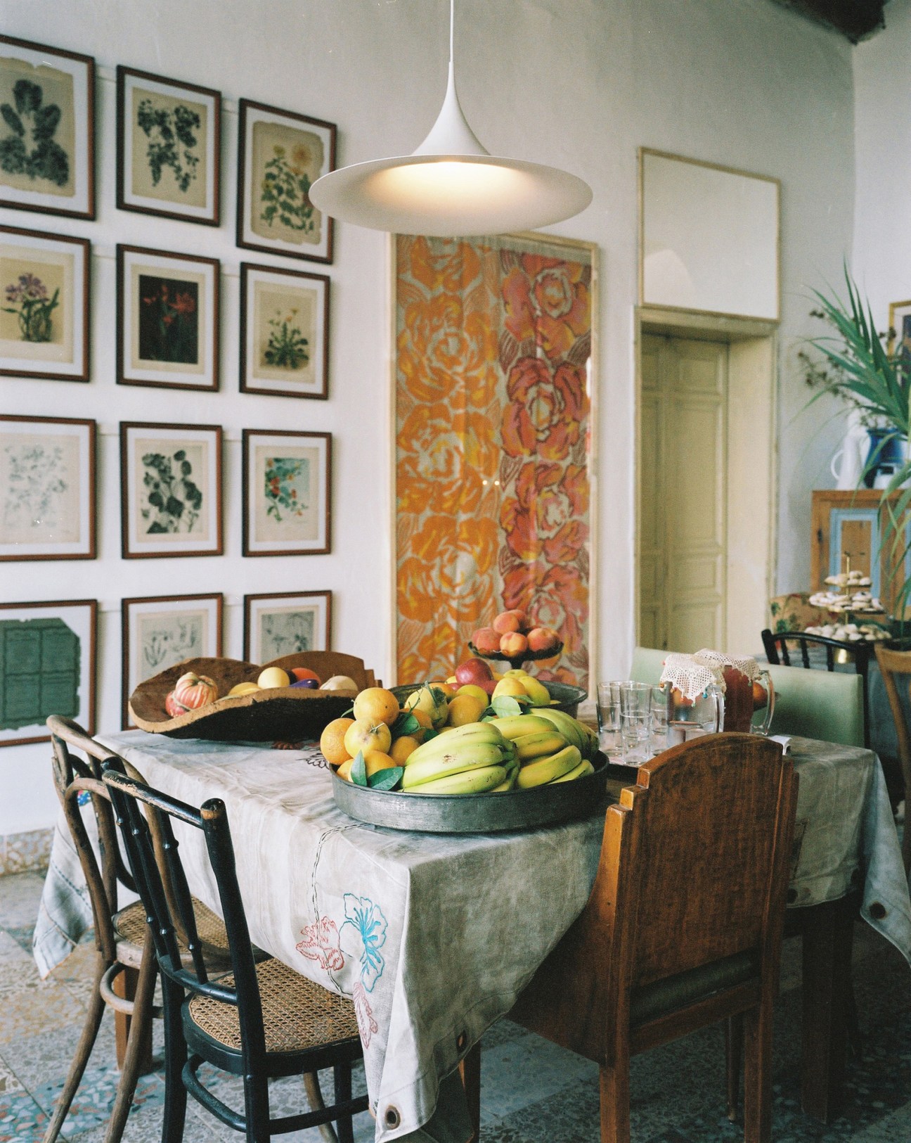 A dining table displays fresh fruit and produce bowls beneath botanical prints and a pendant light at Beit Douma.