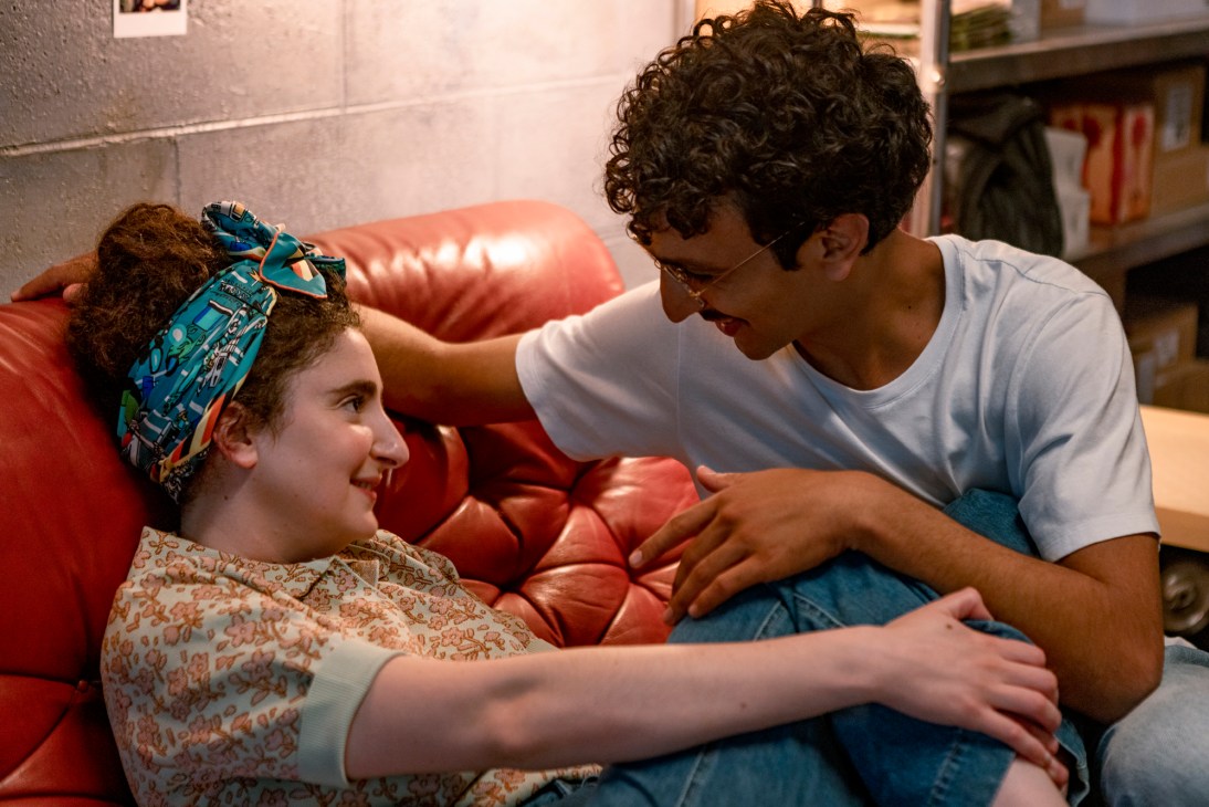 Two people sitting close together on a red leather couch in an intimate scene from Standing Up