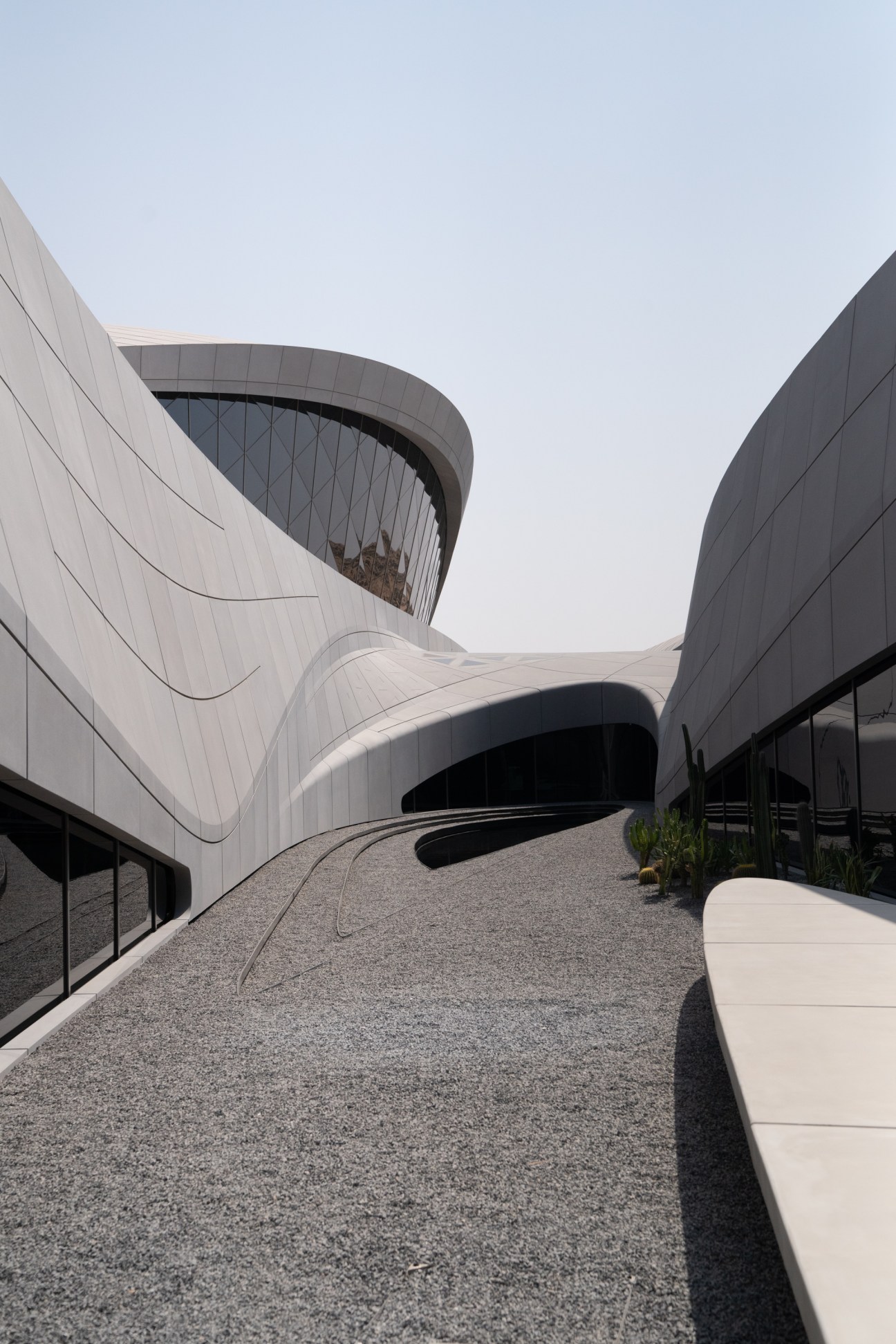 Beeah HQ's curved white concrete facade with organic undulating forms and integrated glass windows in a desert courtyard.