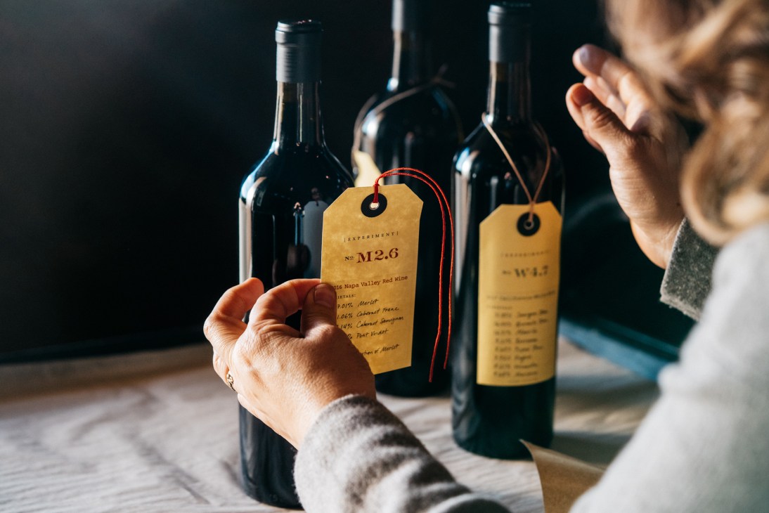 Person examining wine bottles with yellow tags from Ovid Napa Valley winery for mail-order preparation