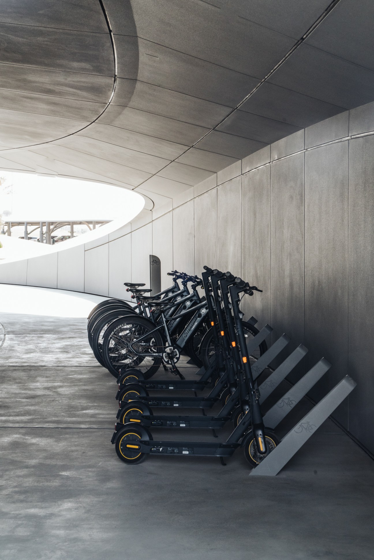 Electric scooters and bicycles parked in a curved concrete garage at Beeah HQ.